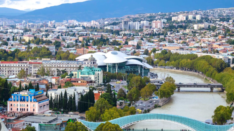 High-rise commercial skyline in Tbilisi and Batumi waterfront with digital blockchain network overlay graphics.