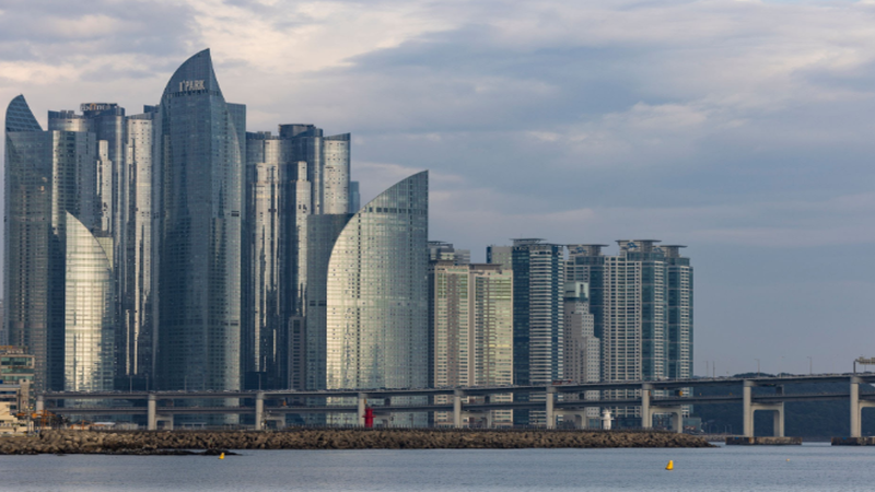 A luxurious architectural view of Haeundae Marine City and Gwangan Bridge skyline in Busan integrated with digital blockchain network overlay graphics.