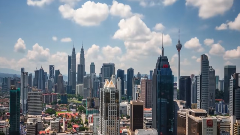 Illuminated panoramic skyline of Kuala Lumpur with Petronas Twin Towers and TRX financial center overlaid with digital blockchain security token network graphics.