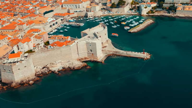 Panoramic view of Dubrovnik's historic walled Old Town and the Adriatic Sea at sunset, overlaid with digital blockchain nodes and Euro-stablecoin yield charts.